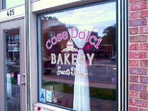 A bakery storefront window displays the name "Cose Dolci Bakery" with a pink and gold design.