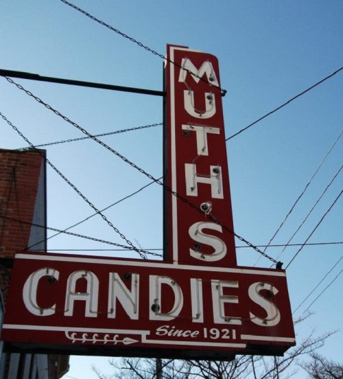Vintage sign for Muth's Candies, established in 1921, against a clear blue sky.