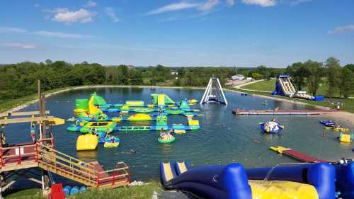 A vibrant water park with inflatable structures on a lake, surrounded by greenery and blue skies.