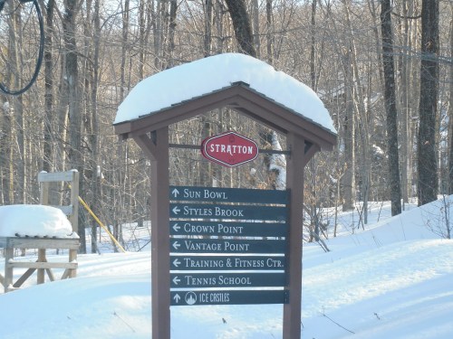 Signpost in a snowy landscape, listing directions to various locations at Stratton, including Sun Bowl and Tennis School.
