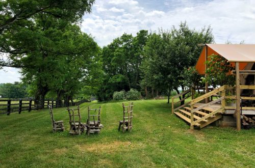 A grassy area with wooden chairs arranged near a rustic building and trees under a partly cloudy sky.
