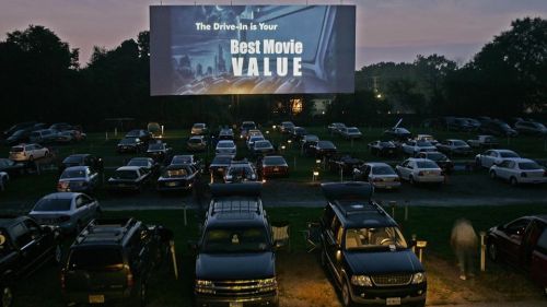 A drive-in movie theater with cars parked in front of a large screen displaying "Best Movie Value."