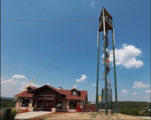A tall spiral climbing tower next to a rustic building under a blue sky with scattered clouds.