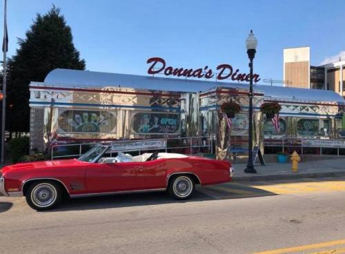 A shiny red convertible parked in front of Donna's Diner, a retro-style diner with a chrome exterior.