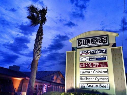 Sign for Miller's Seafood & Steakhouse at dusk, featuring menu items and a palm tree against a cloudy sky.