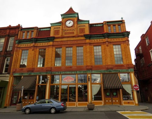 Historic brick building with a clock tower, featuring large windows and striped awnings, located in a downtown area.