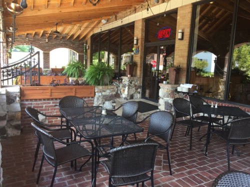 Outdoor dining area with black tables and chairs, stone accents, and large windows. "Open" sign visible.