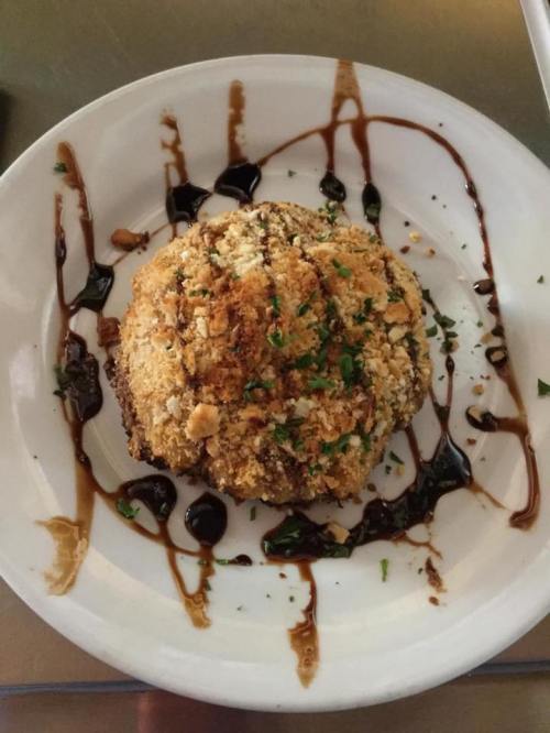 A round, breaded and fried dish drizzled with balsamic glaze and garnished with parsley on a white plate.