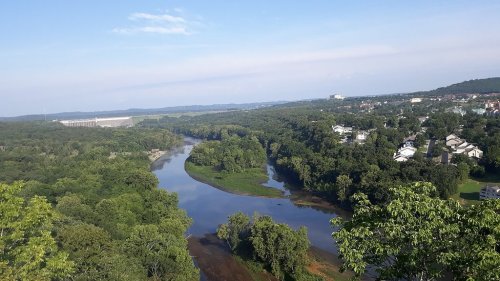 A scenic view of a river winding through lush green trees and a small town under a clear blue sky.