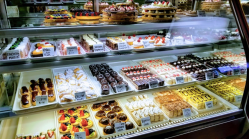 A display case filled with various colorful pastries and desserts, including cakes, tarts, and cream-filled treats.