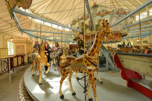 A vintage carousel with colorful horses and giraffes, featuring people enjoying a ride in a bright, airy setting.