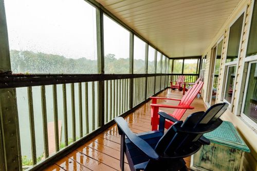 A covered porch with red and black chairs, overlooking a rainy landscape through large windows.
