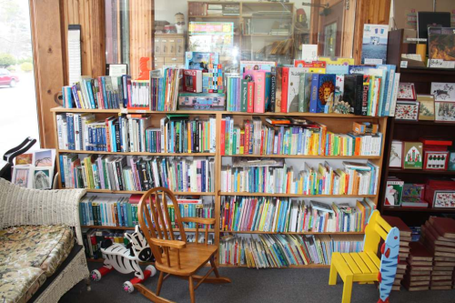 A cozy library corner with two wooden bookshelves filled with colorful books and a small chair in front.