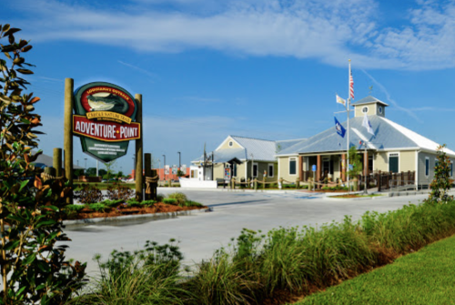 A building with a sign reading "Adventure Point," surrounded by greenery and a clear blue sky.