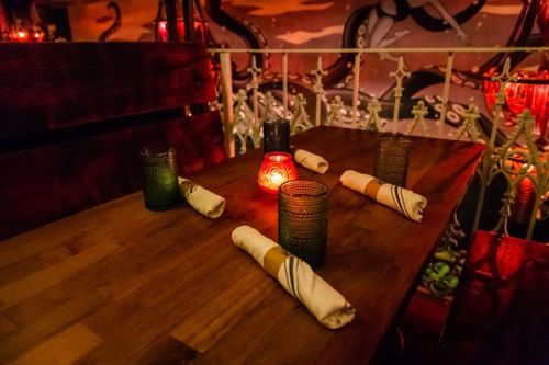 A dimly lit table set for dining, featuring candles and neatly rolled napkins in a cozy restaurant atmosphere.