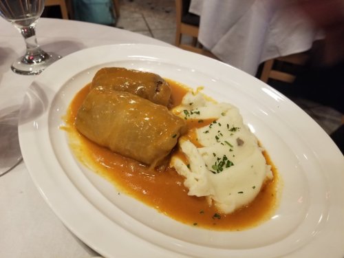 A plate featuring two stuffed cabbage rolls in sauce, served alongside creamy mashed potatoes garnished with herbs.