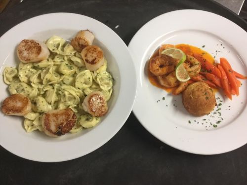 Two plates of gourmet food: one with tortellini and scallops, the other with shrimp, cornbread, and carrots.