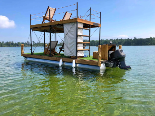 A floating structure on a lake with wooden chairs, a staircase, and a motor at the back, surrounded by clear water.