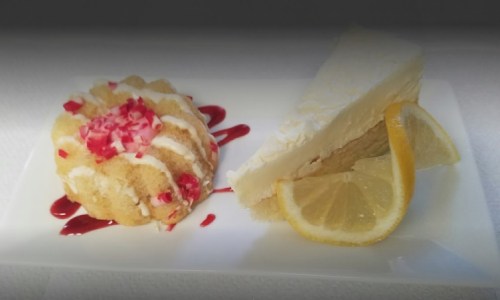 A plate featuring a small cake topped with red sprinkles and a slice of lemon cheesecake with lemon wedges.