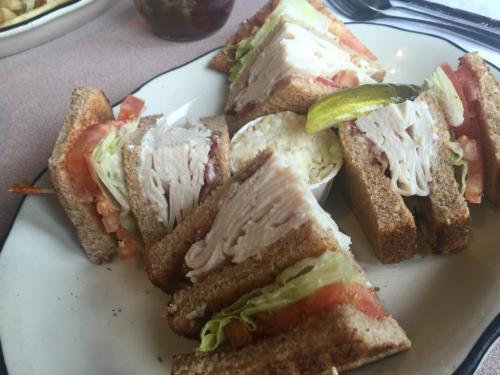 A plate of turkey sandwiches on whole grain bread, layered with lettuce, tomato, and pickles.