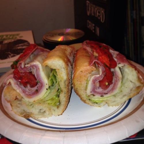 A sandwich cut in half, filled with layers of meats, lettuce, and roasted red peppers on a plate.