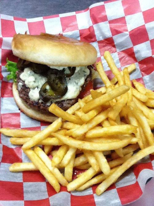 A burger with lettuce, jalapeños, and sauce on a red and white checkered plate, served with a side of golden fries.