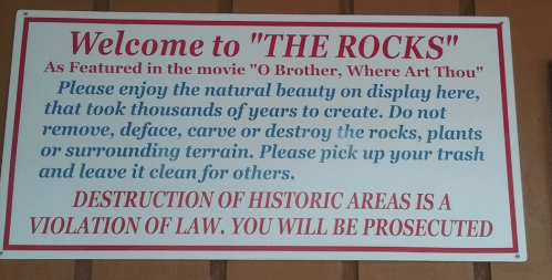 Sign welcoming visitors to "The Rocks," highlighting natural beauty and rules against damaging the area.