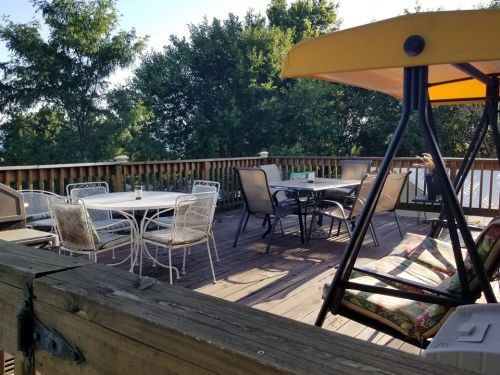 A spacious wooden deck with outdoor furniture, including tables, chairs, and a swing, surrounded by trees.
