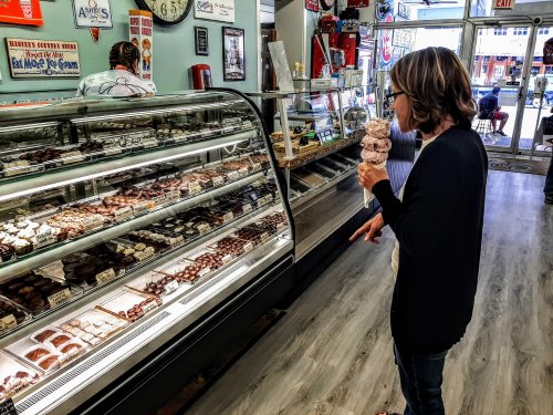 A woman with an ice cream cone points at a display of desserts in a vintage-style ice cream shop.