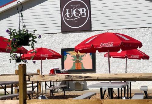 Outdoor seating area with red umbrellas, a mural, and a sign for Uncle Bert's, featuring a rustic wooden fence.