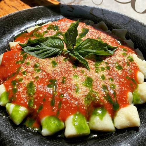 A plate of gnocchi topped with red sauce, green pesto, grated cheese, and fresh basil leaves.