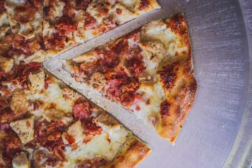 A close-up of a pizza with chicken and bacon toppings, featuring a slice partially removed from the whole.