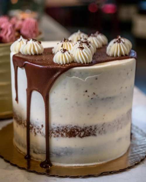 A layered cake with chocolate ganache dripping down, topped with swirls of cream and chocolate shavings.
