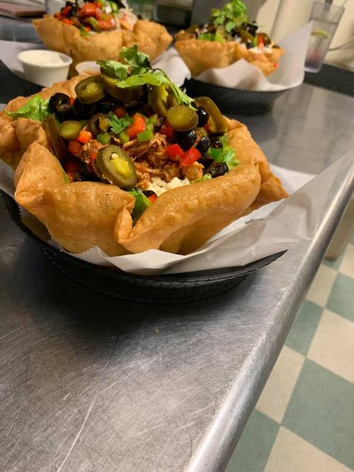 A crispy tortilla bowl filled with shredded meat, olives, jalapeños, and fresh vegetables, garnished with cilantro.