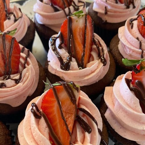Close-up of chocolate cupcakes topped with pink frosting, fresh strawberries, and drizzled chocolate.
