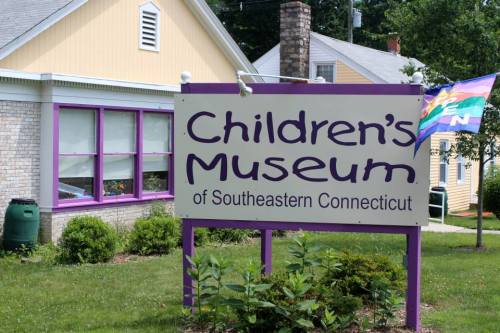 Sign for the Children's Museum of Southeastern Connecticut, featuring purple lettering and a colorful flag in the background.