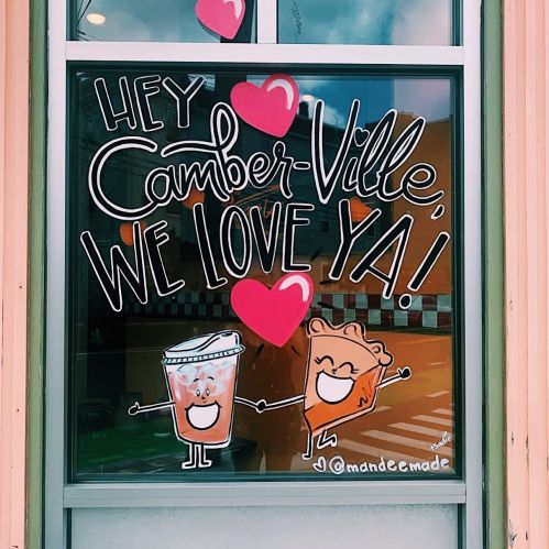 Colorful window mural with text "Hey Camberville, we love ya!" featuring a smiling drink and pastry with hearts.