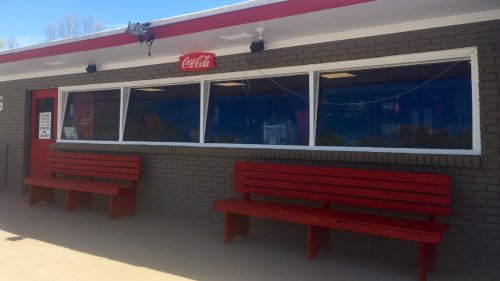 A building with a Coca-Cola sign, featuring large windows and two red benches outside.