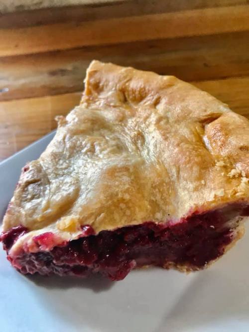 A slice of cherry pie with a flaky crust, revealing a rich, red filling on a white plate.