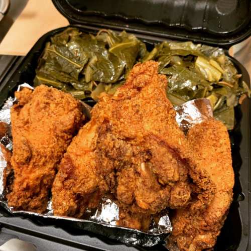 A takeout container with crispy fried chicken and a side of collard greens.