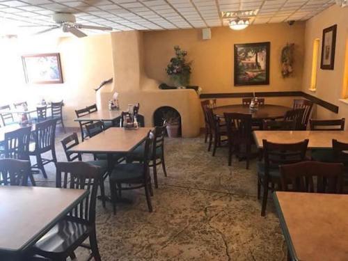 A spacious restaurant interior with empty tables and chairs, featuring a warm color scheme and decorative wall art.
