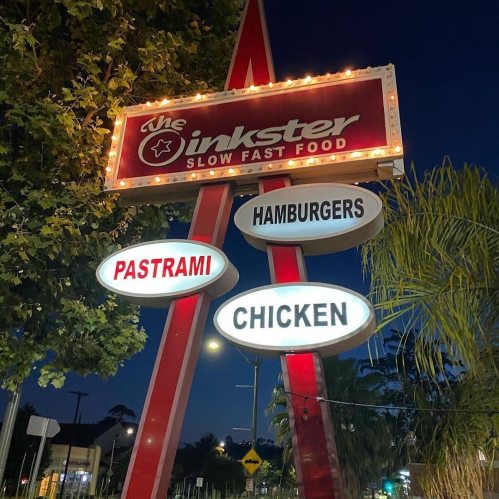 A retro-style sign for "The Inkster" featuring lights, advertising pastrami, hamburgers, and chicken at night.