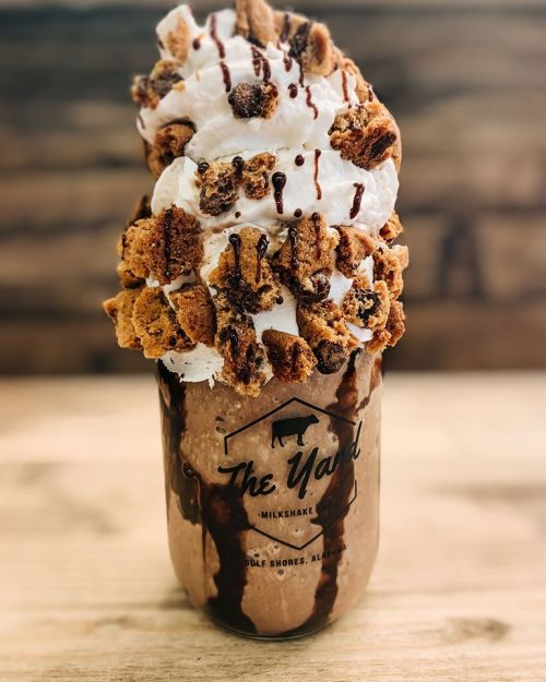 A decadent milkshake topped with whipped cream, cookie crumbles, and chocolate drizzle in a branded glass jar.