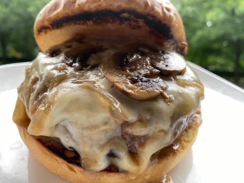A close-up of a juicy burger topped with melted cheese and sautéed mushrooms, served on a toasted bun.