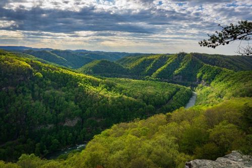 A panoramic view of lush green mountains and a winding river under a cloudy sky.