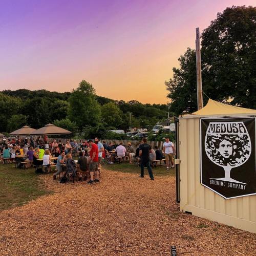 A lively outdoor gathering at Medusa Brewing Company during sunset, with people enjoying drinks and conversation.