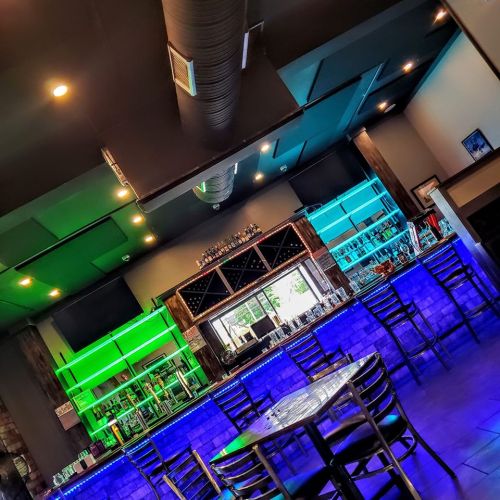 A modern bar interior with colorful LED lighting, featuring a sleek counter and empty tables.
