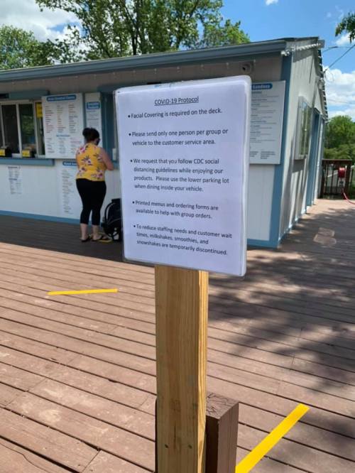 Sign detailing COVID-19 protocols, including mask requirements and social distancing guidelines, near a customer service area.