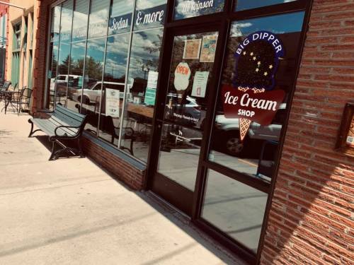 A storefront with a sign reading "Big Dipper Ice Cream Shop," featuring large windows and a bench outside.