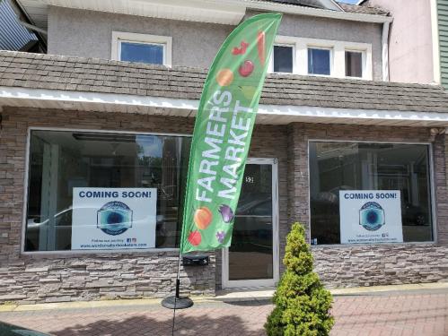 A storefront with a green flag reading "FARMERS MARKET" and signs saying "COMING SOON" in the windows.